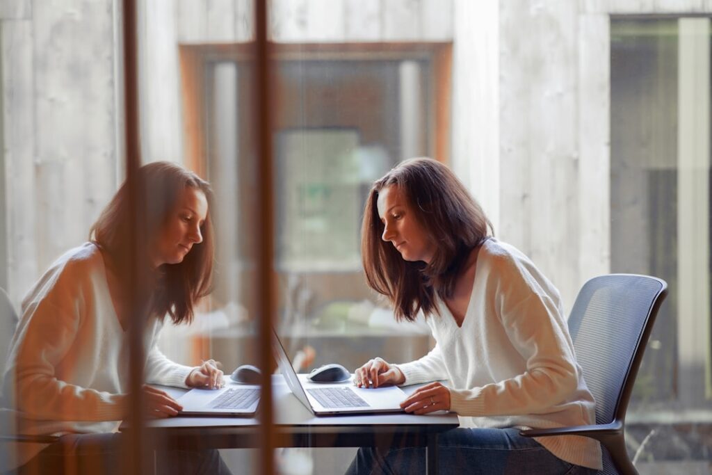 A woman working at a laptop in a startup office, standing in a modern meeting room with her reflection.