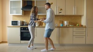 Attractive young joyful couple have fun dancing while cooking in the kitchen at home in the morining