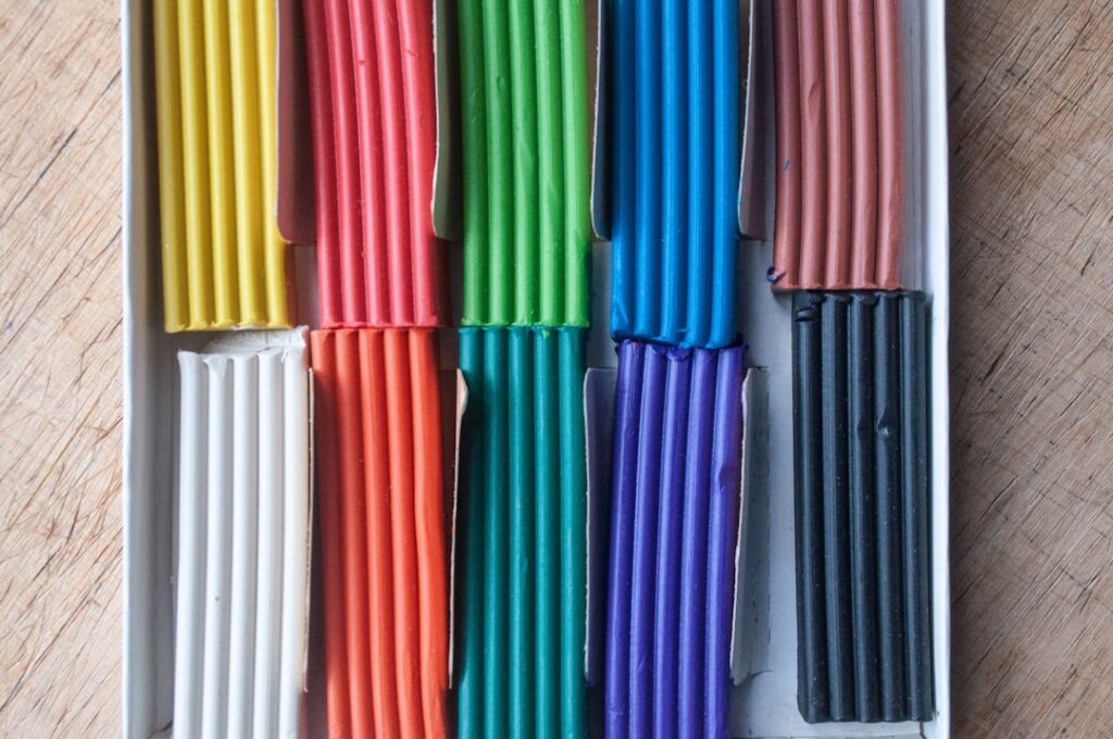 Top view box of colorful plasticine on wooden table background. Modelling clay package.